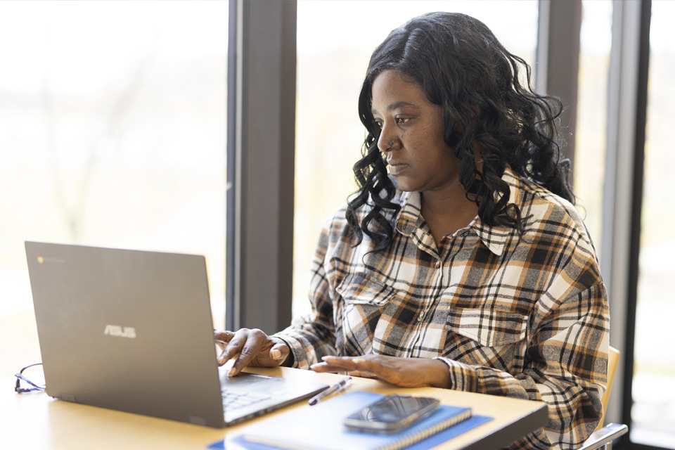 Black female student sitting at a table with a laptop working on her resume