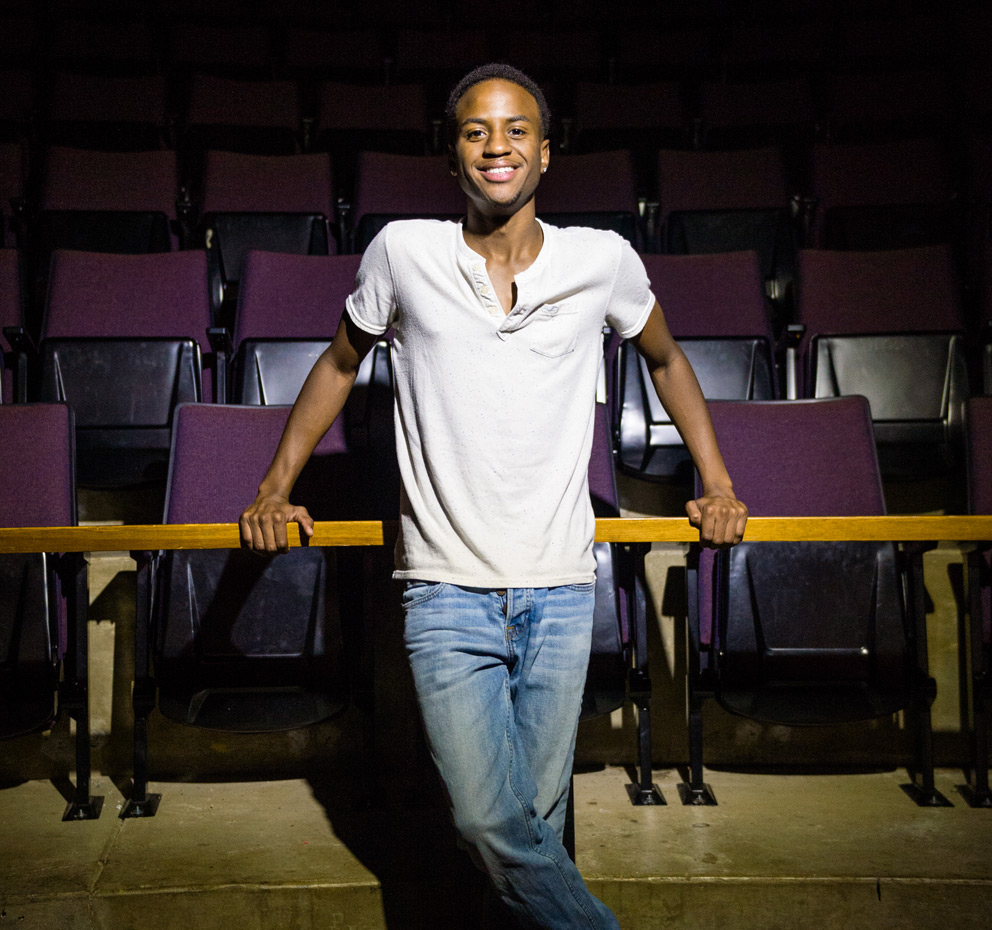 Black male student standing in theatre under spotlight